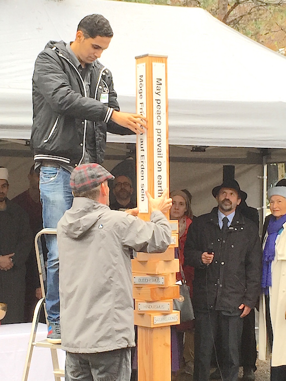 der gemeinsame Friedenspfahl wird aufgestellt, Holzpfahl mit beschrifteten Elementen, Mann auf Leiter
