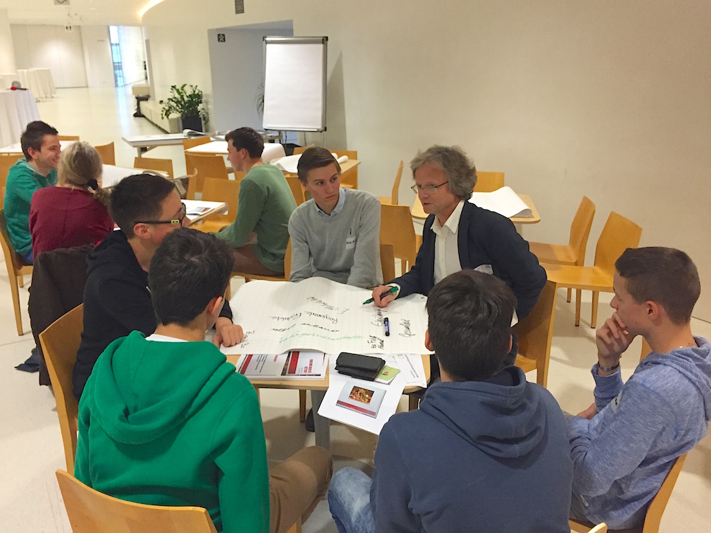Ideensammlung im World Cafe, Jugendgruppe am Tisch, Moderator notiert Ergebnisse